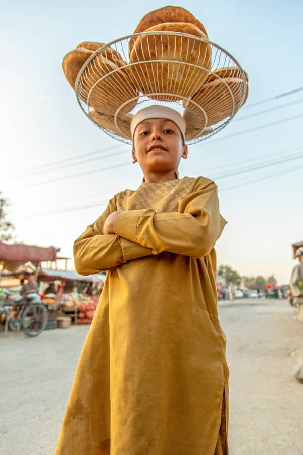 A boy in Afghanistan carries bread in a basket on his head.